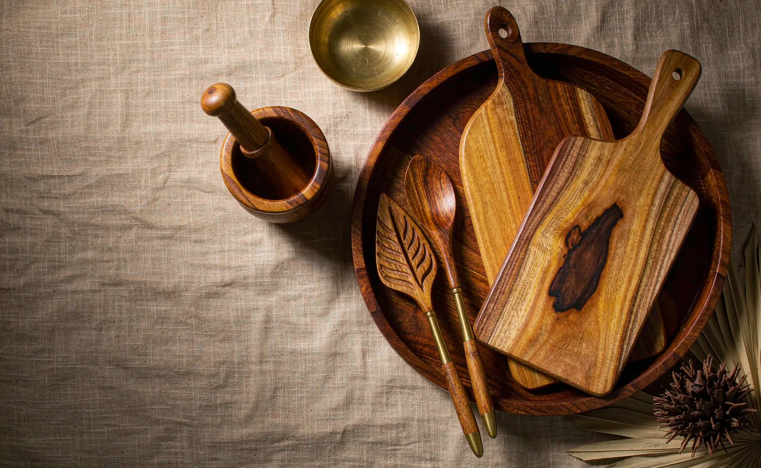 Teak kitchenware laid out on linen: chopping boards, a round tray, a mortar and carved spoons
